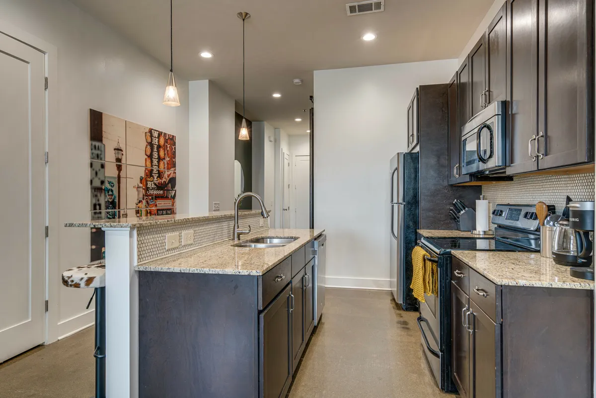 A modern kitchen environment featuring a polished granite countertop, stylish dark cabinetry, essential kitchen appliances, and an eye-catching art piece on the wall. The scene is set for culinary adventures, socializing, and meal preparation, with a clean and functional aesthetic.