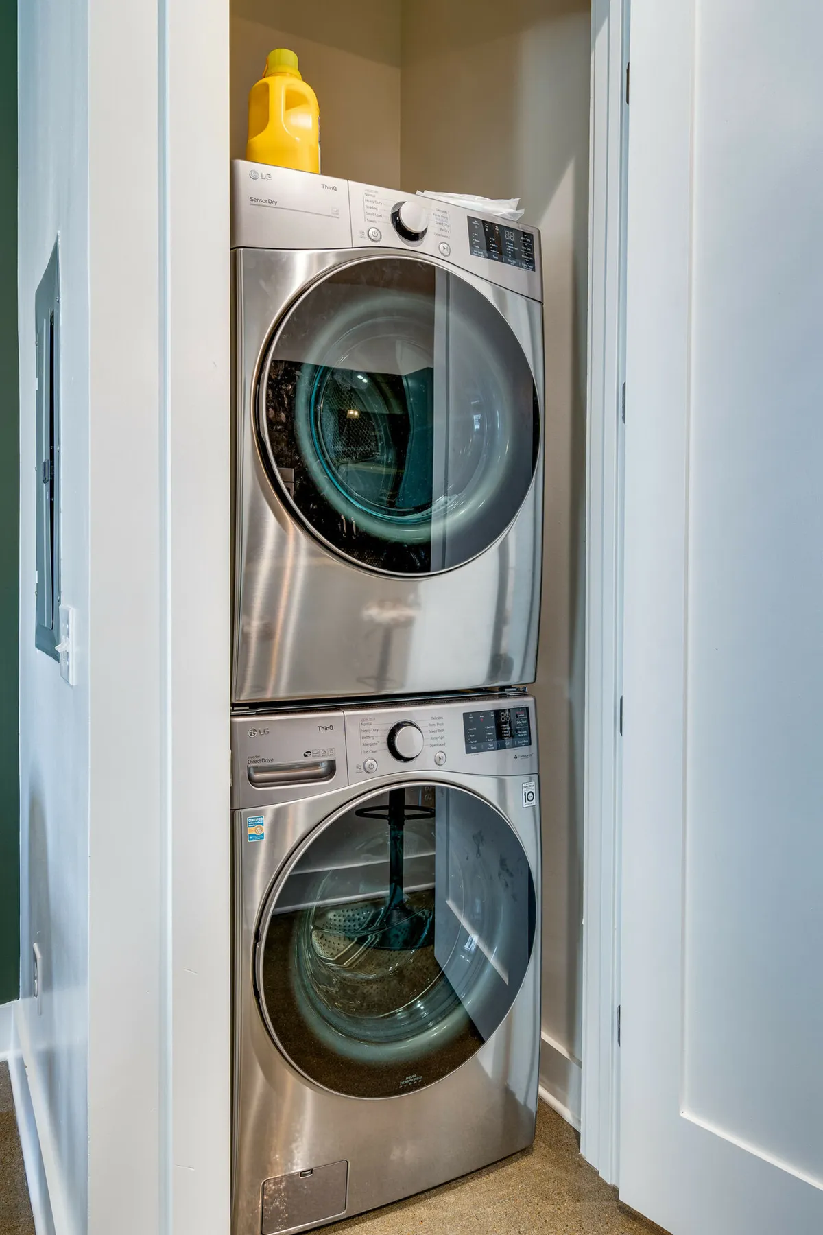 This image features a stacked washer and dryer set within a clean and organized laundry area. A bottle of laundry detergent sits atop the machine, emphasizing convenience and modern amenities available to guests.