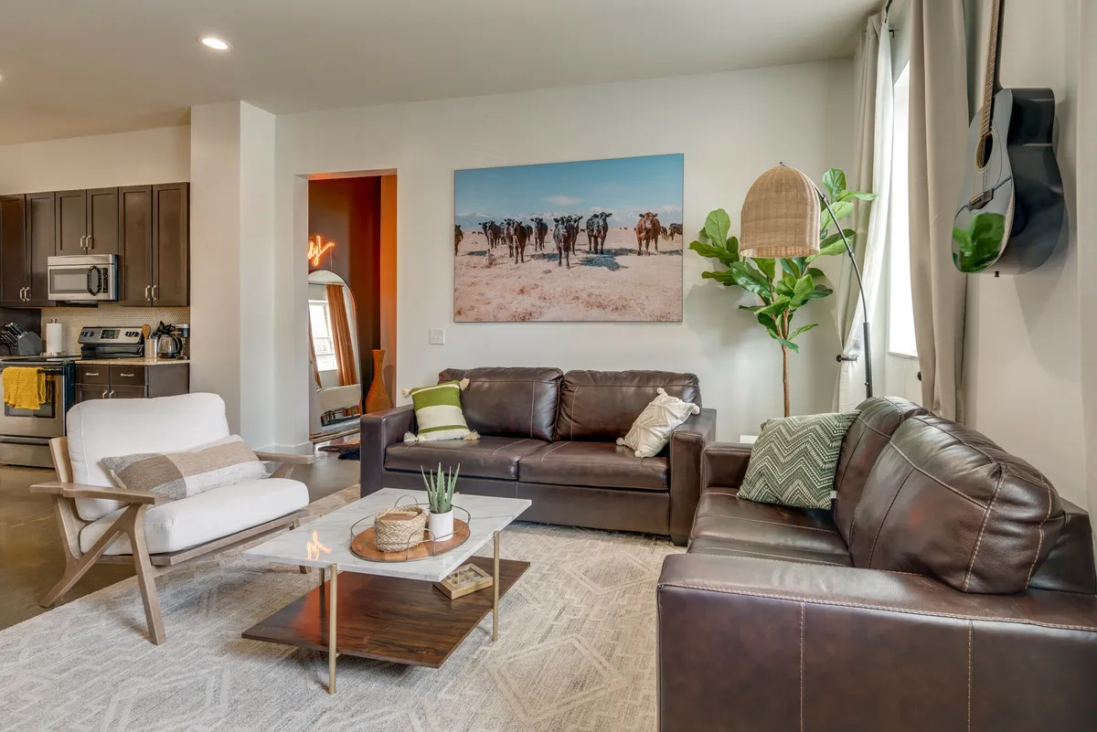 A spacious living lounge featuring leather sofas, a central coffee table, vibrant wall art, and an indoor plant. The setup encourages relaxation, socializing, and entertaining, all under abundant natural light.