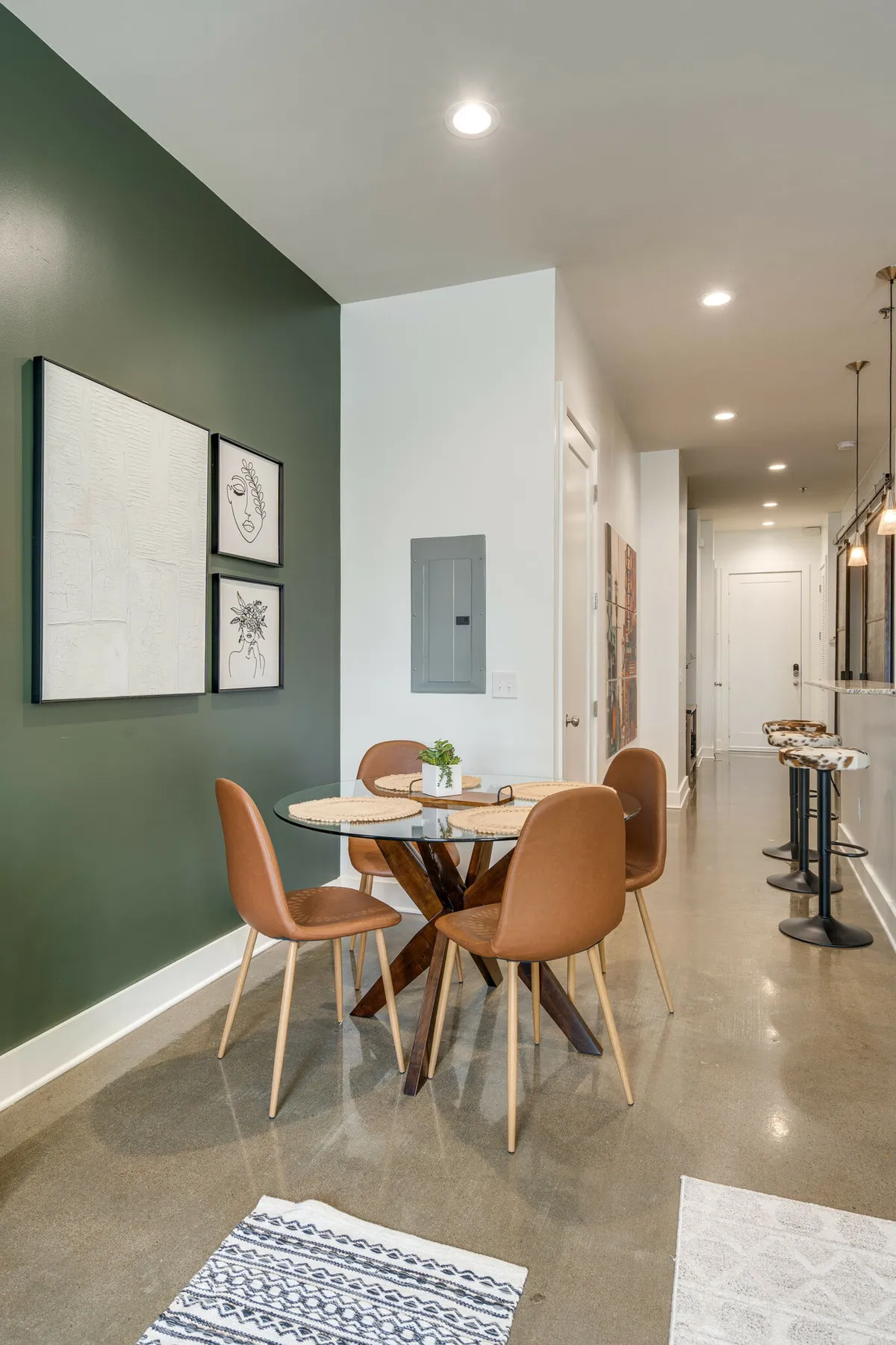 A contemporary dining area anchored by a sleek table, comfortable bar stools, and vibrant artwork on the wall. The setting is ideal for casual dining, social gatherings, or working remotely, with a warm and inviting ambiance designed for laughter-filled meals or productive mornings.