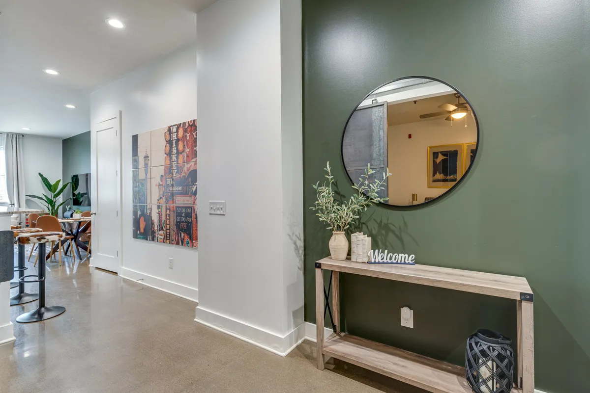 A welcoming entryway with a round mirror, console table, distinctive wall art, and a green accent wall. The area is styled for first impressions, setting the tone for a thoughtfully managed property.