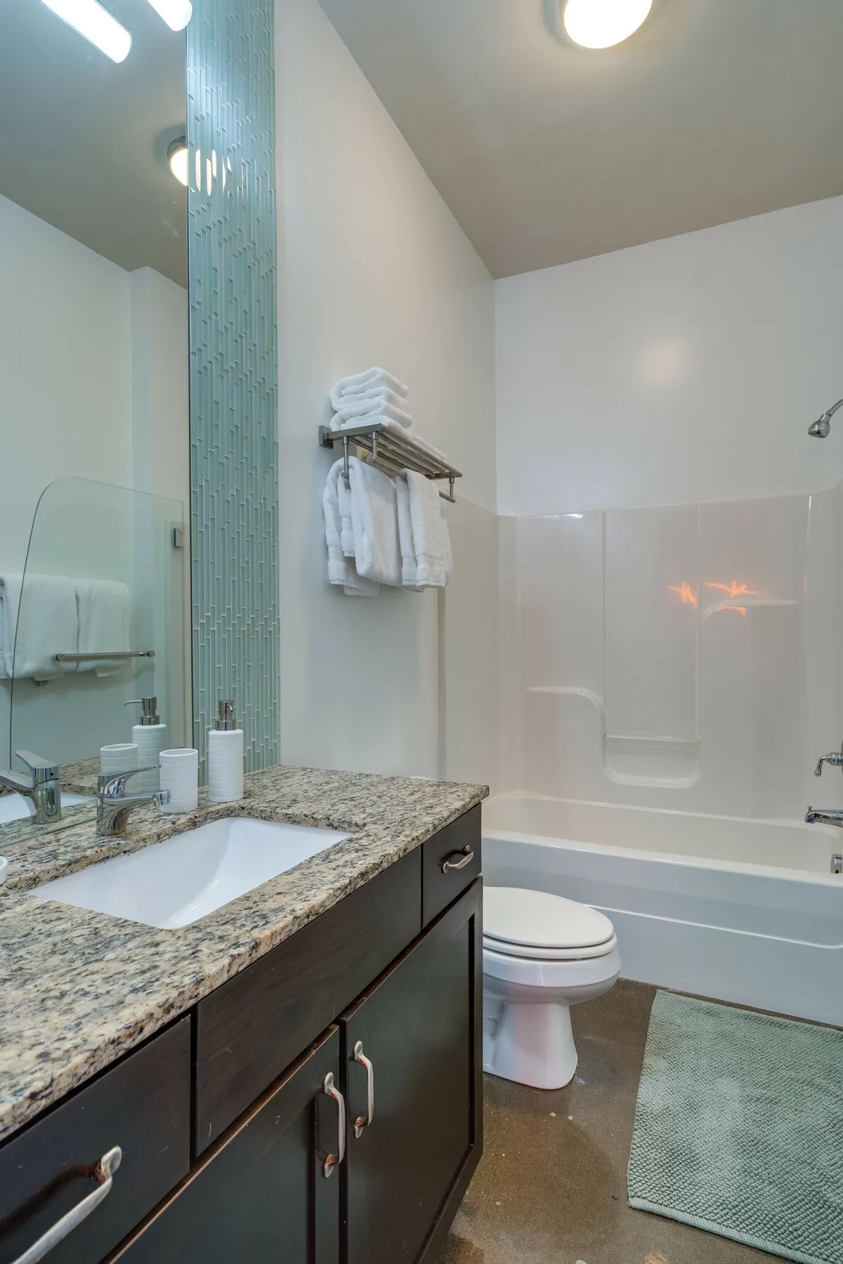 A modern bathroom with a sleek granite countertop, glass shower door, plush towels on a rack, and a contemporary faucet. The space feels serene and well-appointed, suggesting a focus on comfort and cleanliness.